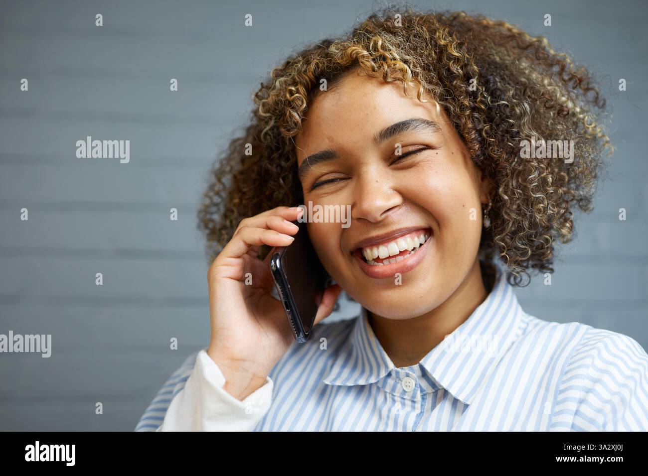 Fröhliche Frau lächelt und spricht auf einem Smartphone in einer ungezwungenen Umgebung Stockfoto