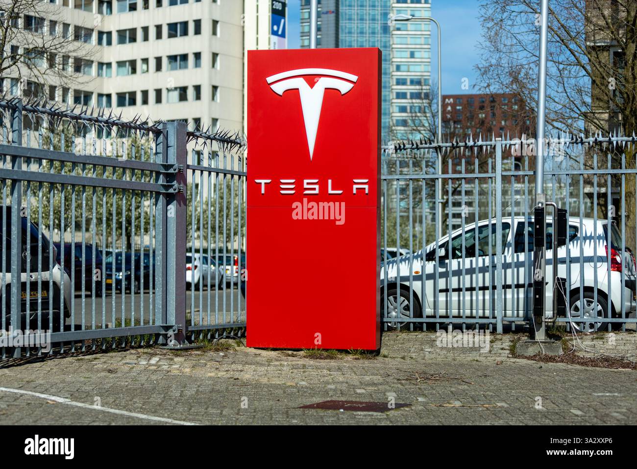 Tesla-Logo-Schild auf einer roten Säule, umgeben von einem Zaun. Stockfoto