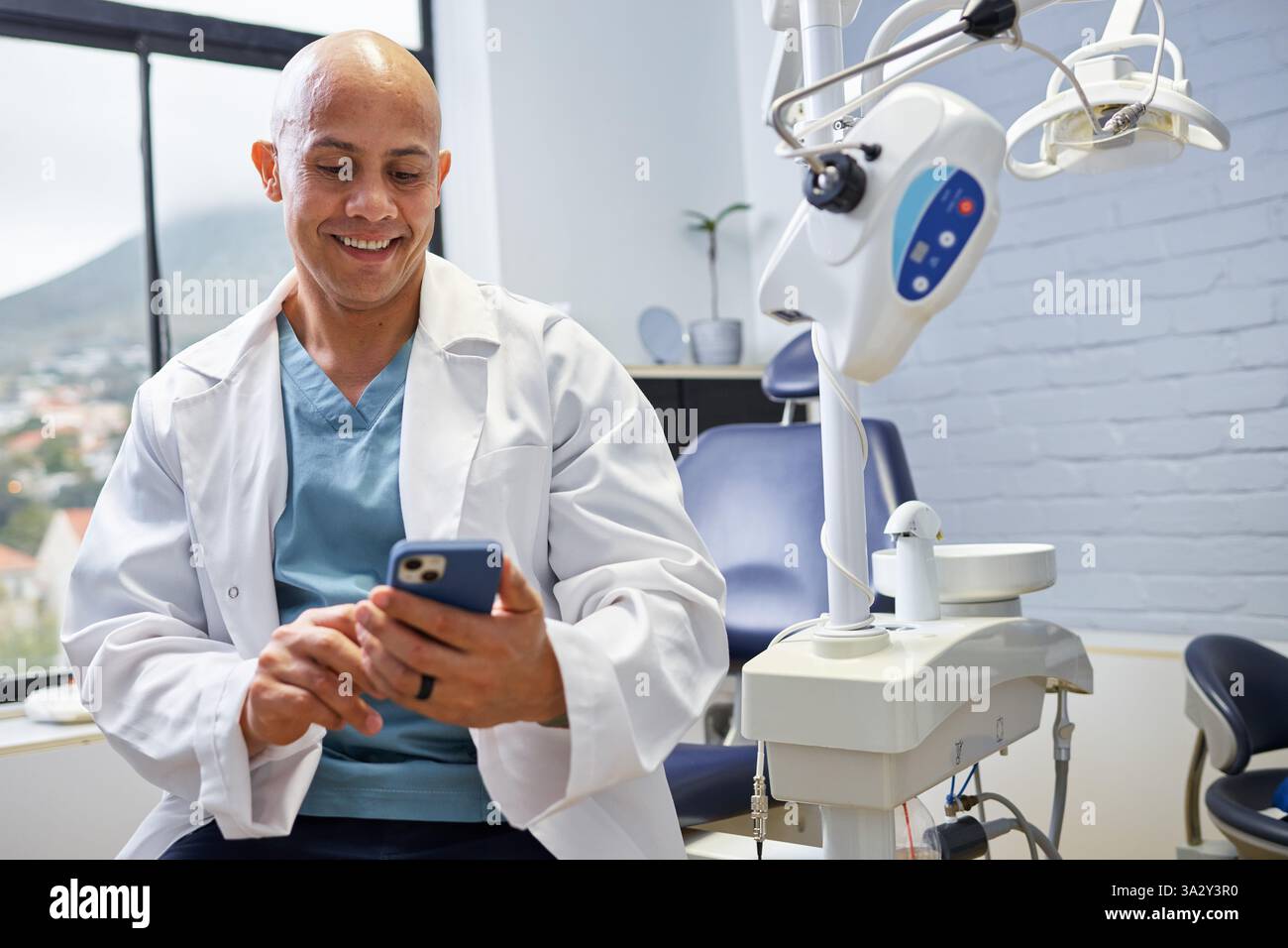 Lächelnder Zahnarzt mit Smartphone in einer modernen Zahnarztpraxis in der Pause Stockfoto
