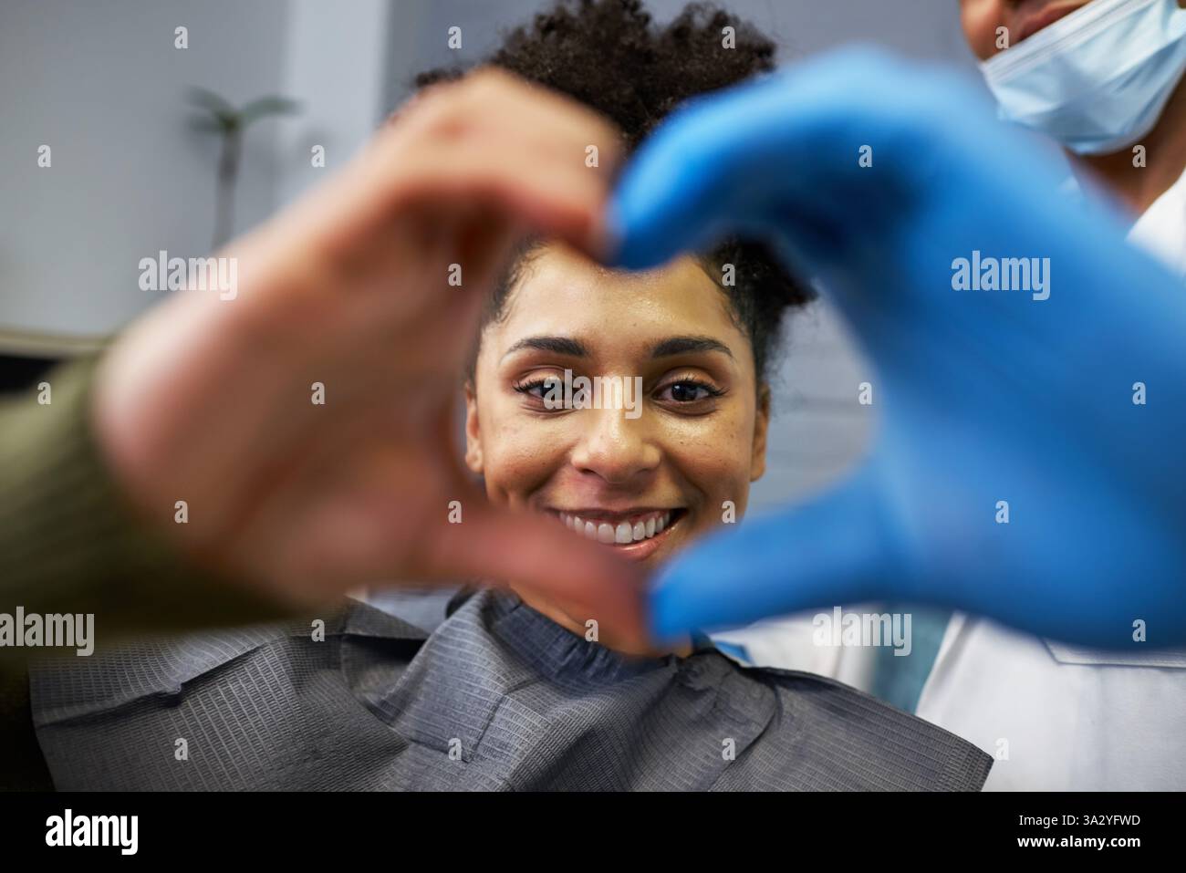 Patient lächelt beim Zahnarztbesuch, eingerahmt von Herzen der Hände Stockfoto