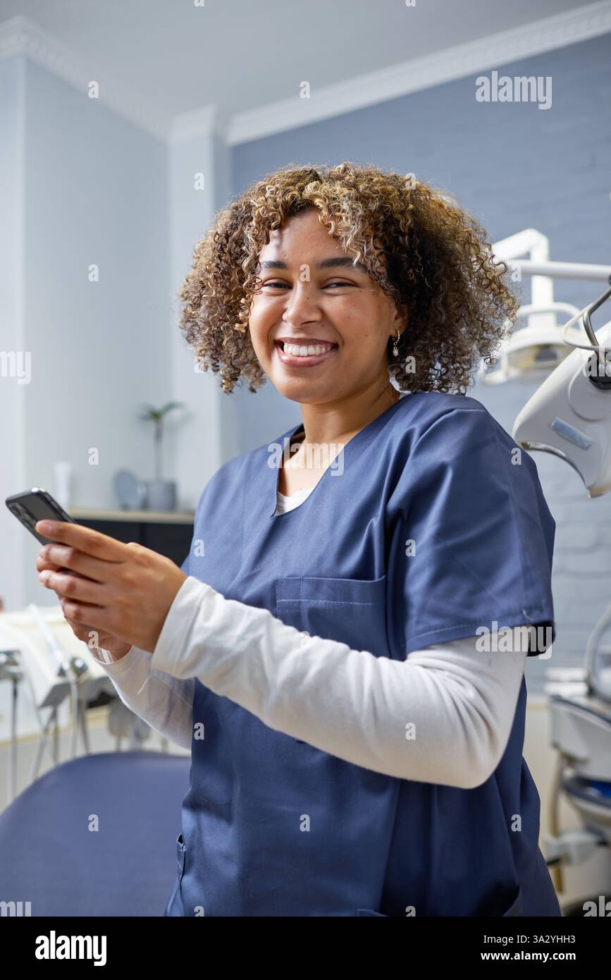 Lächelnder Zahnarzt mit Smartphone in einer modernen klinischen Umgebung Stockfoto
