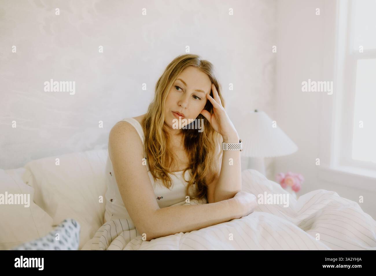 Eine nachdenkliche Frau in ihren 40ern sitzt im Bett, verloren in stiller Besinnung Stockfoto