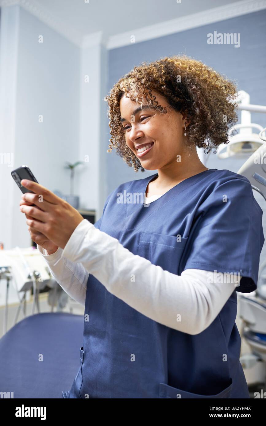 Lächelnder Arzt hält ein Smartphone in einer Zahnarztpraxis Stockfoto