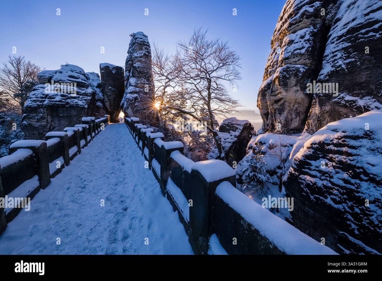 Schneebedeckte Winterlandschaft im Nationalpark Sächsische Schweiz mit der Steinbrücke Bastei Brücke, bei Sonnenaufgang. Stockfoto