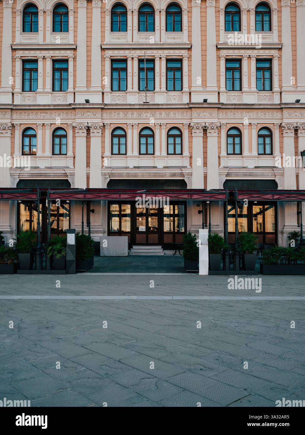 Genießen Sie die atemberaubende Architektur der Piazza Unita d'Italia in Triest, Italien. Der sonnendurchflutete Sommertag hebt die elegante Hotelfassade hervor und zieht die Tour an Stockfoto
