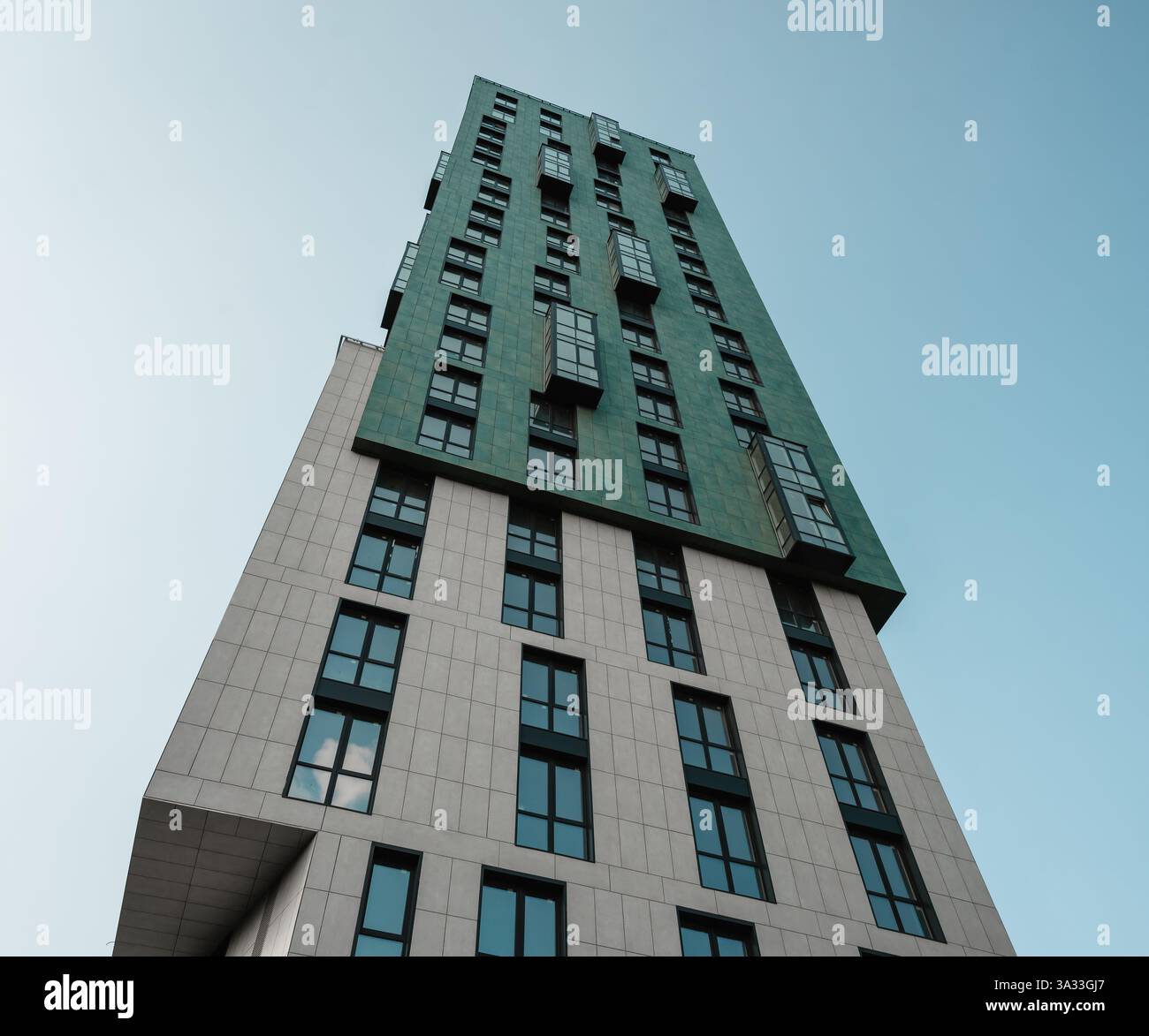 Hochhaus-Wohnturm vor hellblauem Himmel. Blick auf die Fassade eines modernen Gebäudes mit beigefarbener und grüner Fassade. Stockfoto
