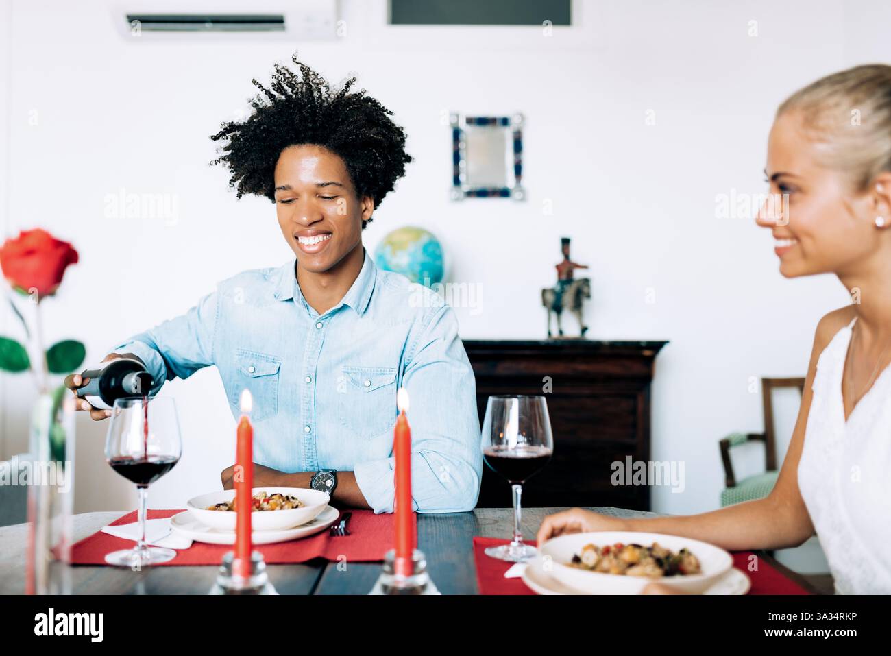 Ein Paar genießt ein romantisches Abendessen mit einem Glas Wein und einem Tisch mit Kerzenschein. Eine Person schenkt Wein und schafft eine warme und intime Atmosphäre. Stockfoto