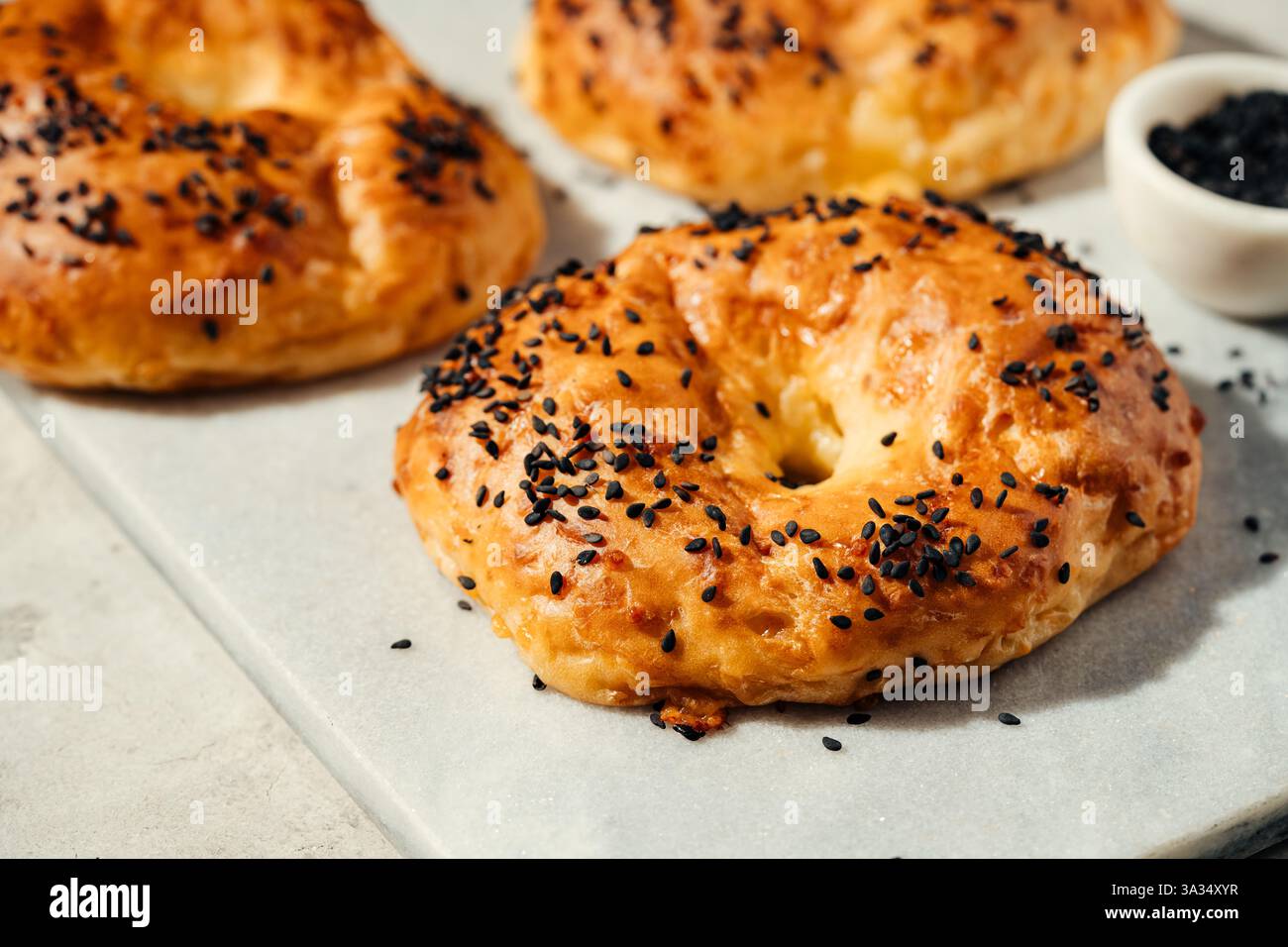 Eine Nahaufnahme goldbrauner Bagels, gekrönt mit schwarzen Sesamsamen, die auf einer weißen Marmorplatte ruhen. Perfekt für Frühstücksszenen, Bäckereiaktionen und Stockfoto