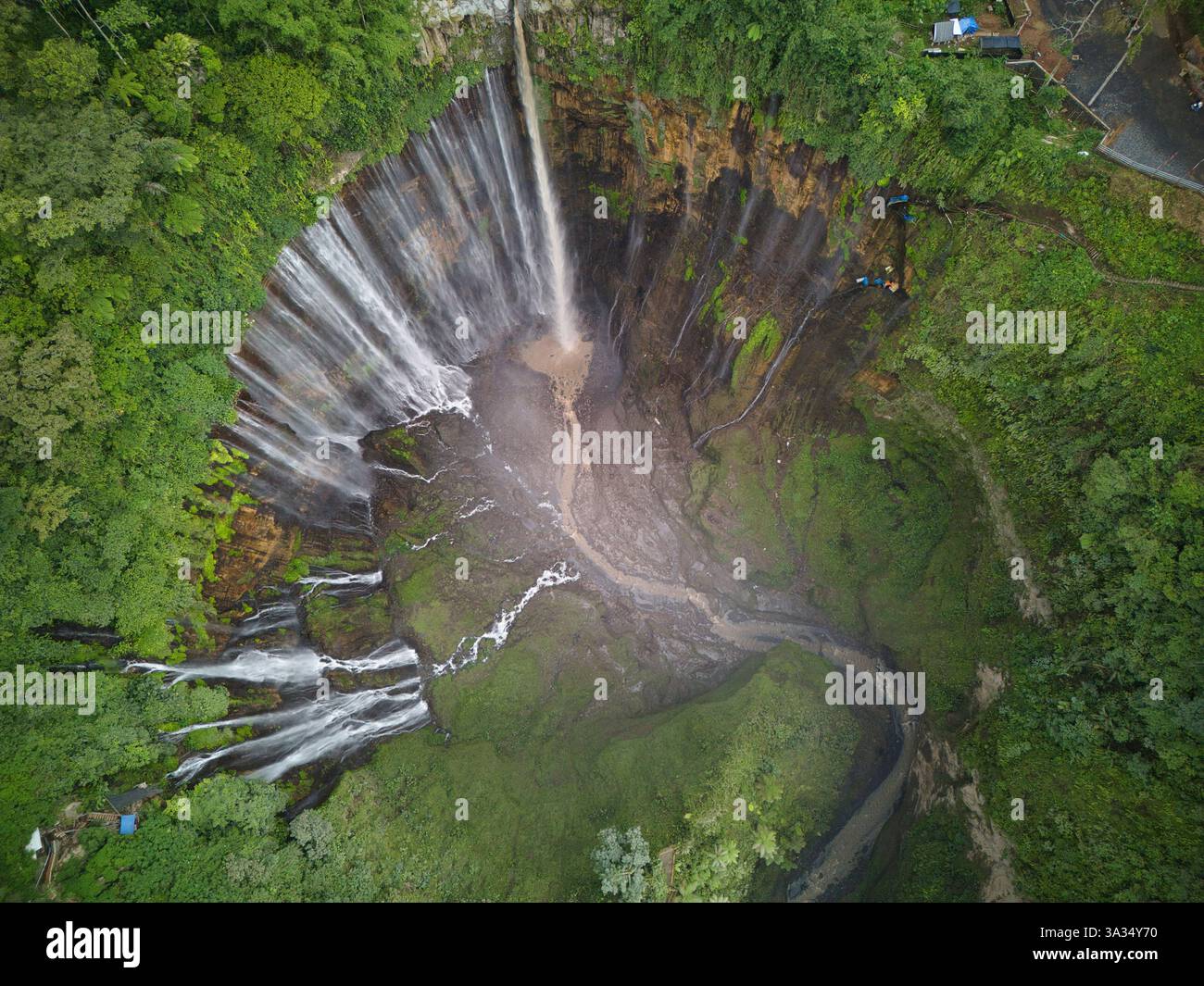 Ein atemberaubendes Luftbild, das den riesigen Tumpak Sewu Wasserfall inmitten eines dichten tropischen Waldes einfängt. Die Kaskade fällt kraftvoll in ein natürliches Stockfoto