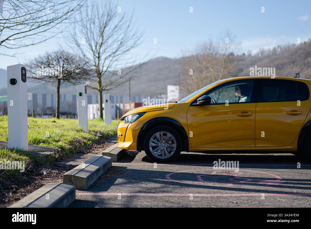 Ein gelbes Elektroauto lädt an einer Station vor einer malerischen Kulisse auf. Das Bild fängt das Wesen nachhaltiger Reisen mit Bäumen im Rücken ein Stockfoto