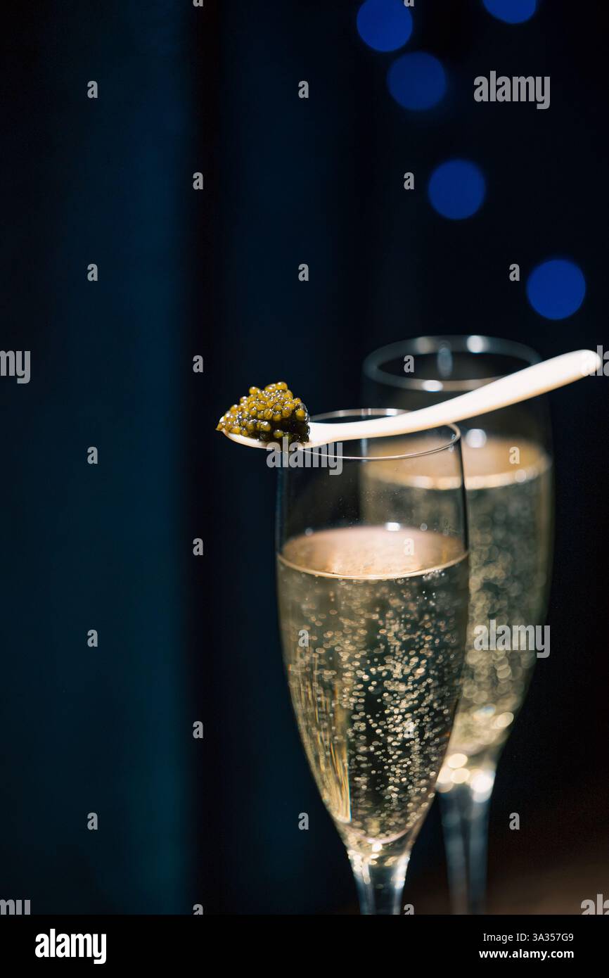 Ein Löffel erstklassiger Beluga-Kaviar auf einem Glas Sekt vor dunklem Hintergrund mit dezenten blauen Lichtern. Stockfoto