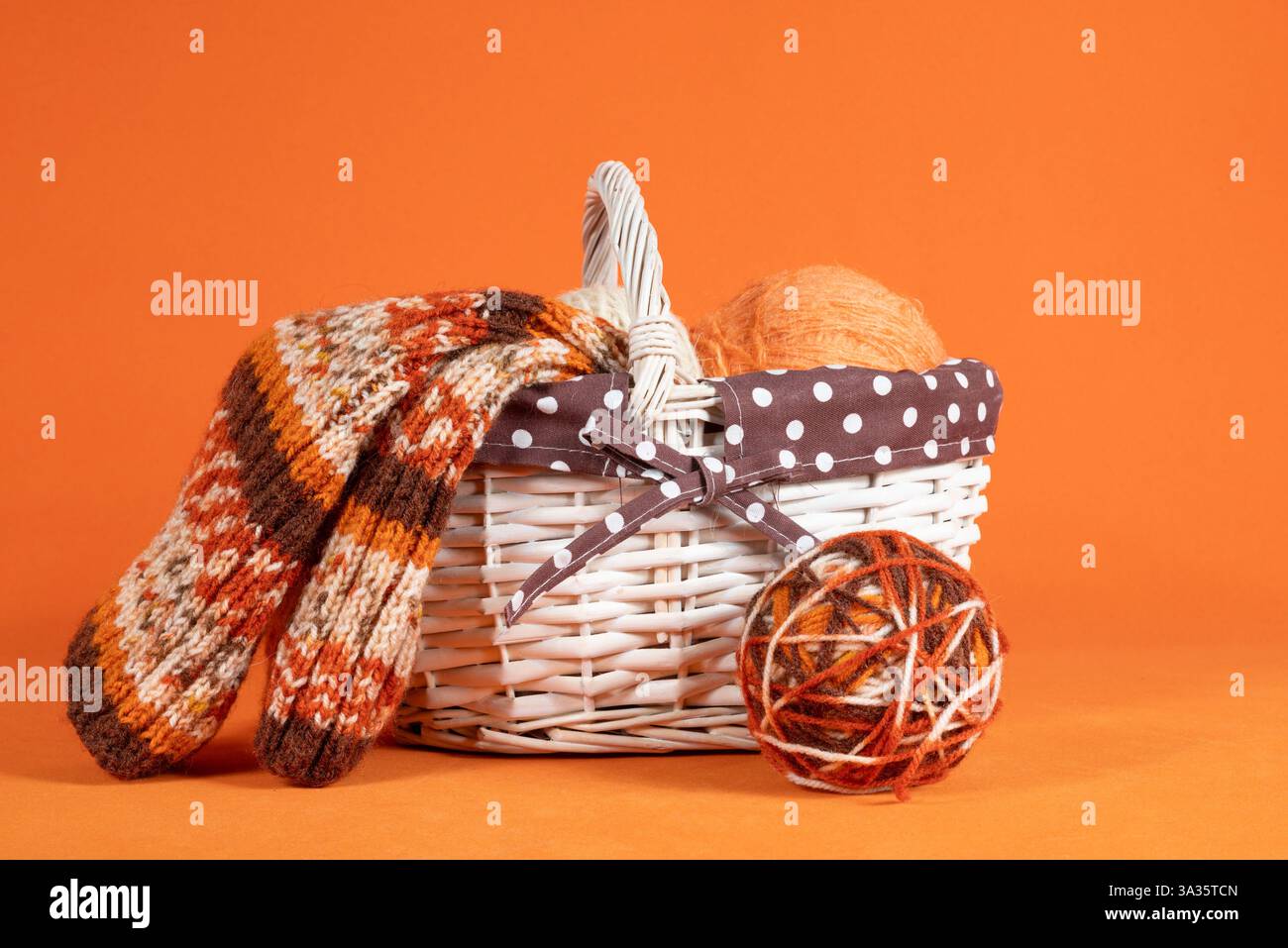 Kugeln aus Wollgarn in verschiedenen Farben in einem Korb, Nahaufnahme auf orangem Hintergrund. Handgefertigte Strickfäden Stockfoto