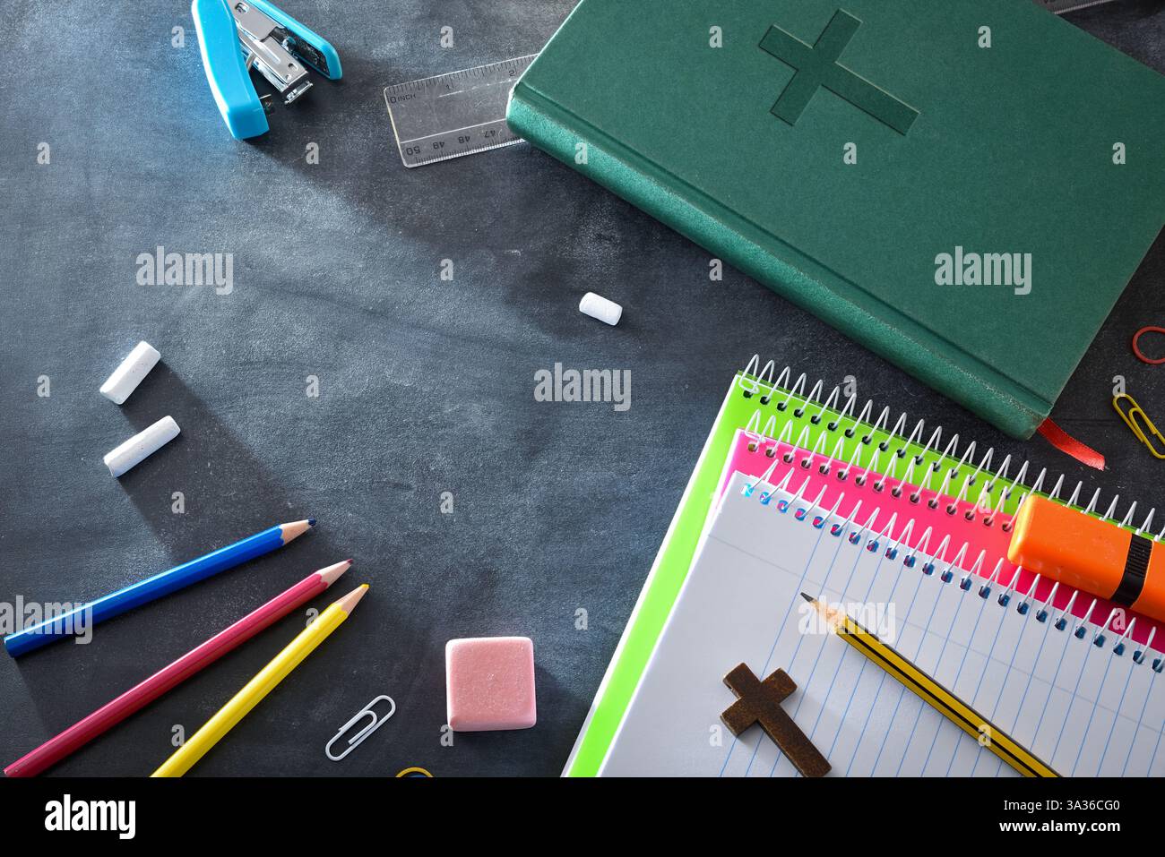 Religiöser pädagogischer Hintergrund mit Schulmaterial auf einer Tafel, wie Notizbücher, Buntstifte, ein Lineal und Radiergummi und eine grüne Bibel. Obere V Stockfoto