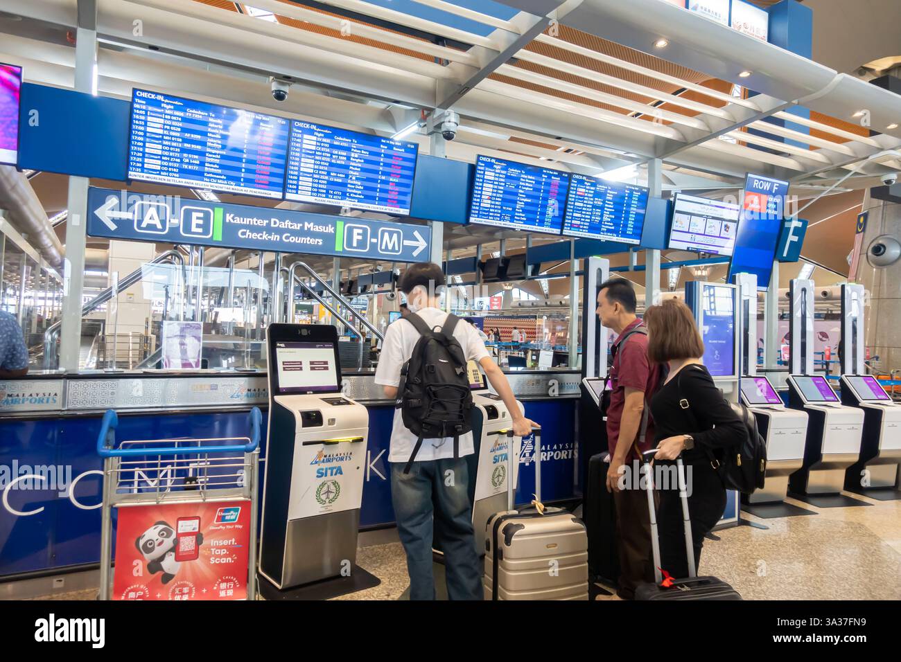 Passagiere an den Check-in-Automaten am internationalen Flughafen Kuala Lumpur (KLIA). Auf mehreren digitalen Bildschirmen werden Fluginformationen angezeigt Stockfoto