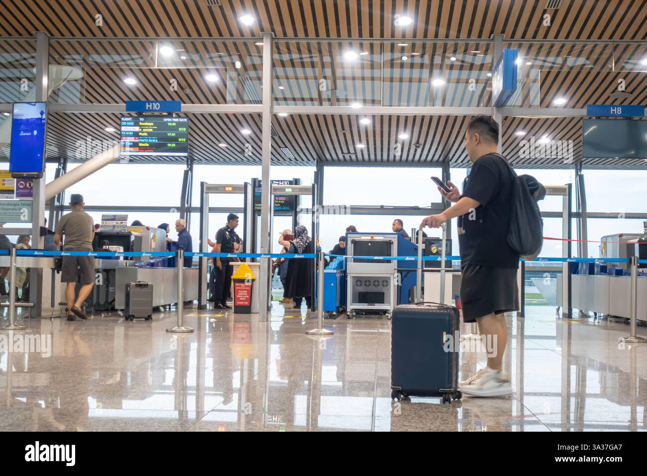 Ein Tourist mit einem rollenden Handgepäckkoffer, der ein Smartphone hält, Sicherheitskontrolle des Handgepäcks, Kuala Lumpur Flughafen, Malaysia Stockfoto
