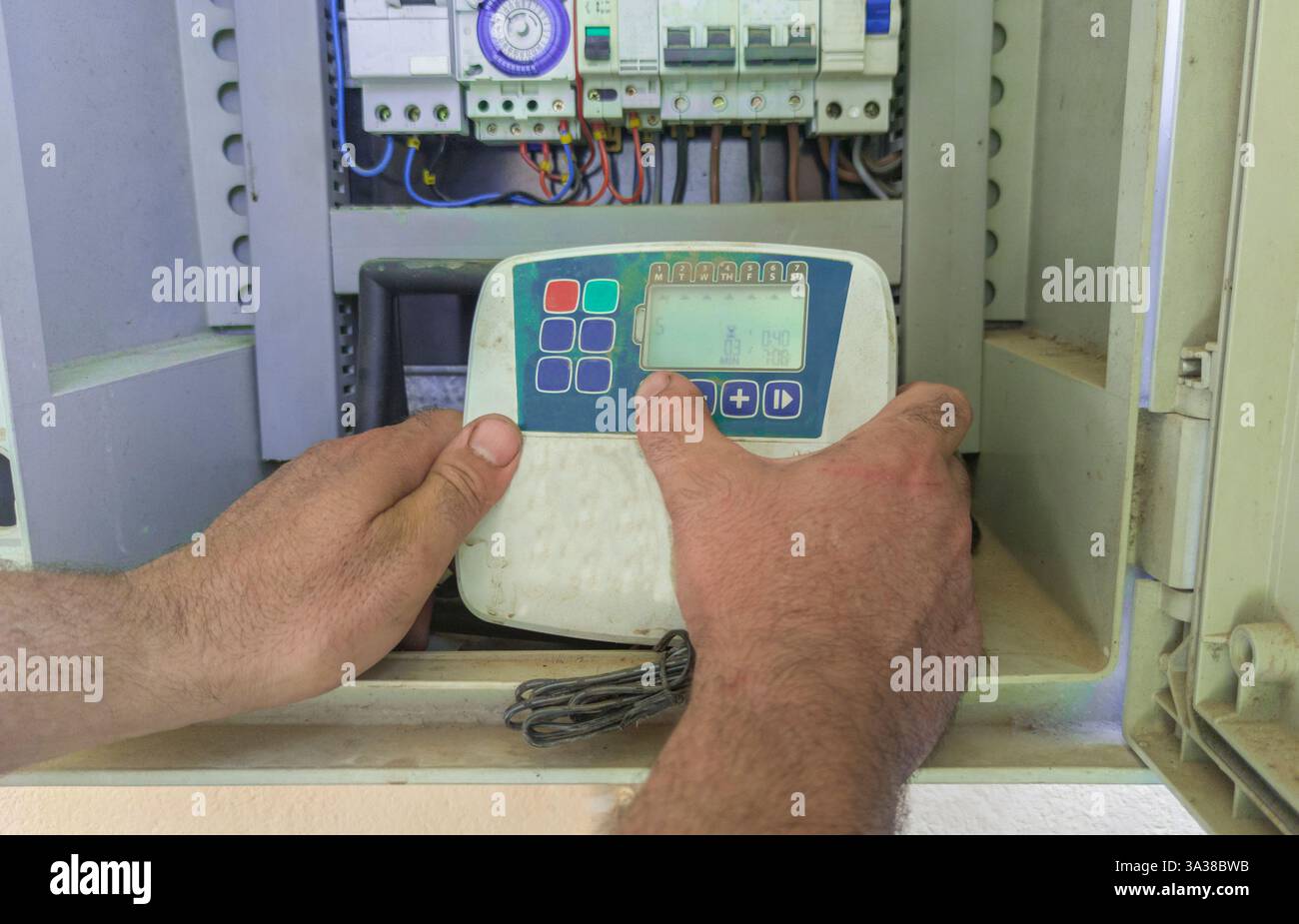 Gärtner programmieren ein automatisches Bewässerungssystem. Manipulation des Gerätes in der elektrischen Schalttafel Stockfoto