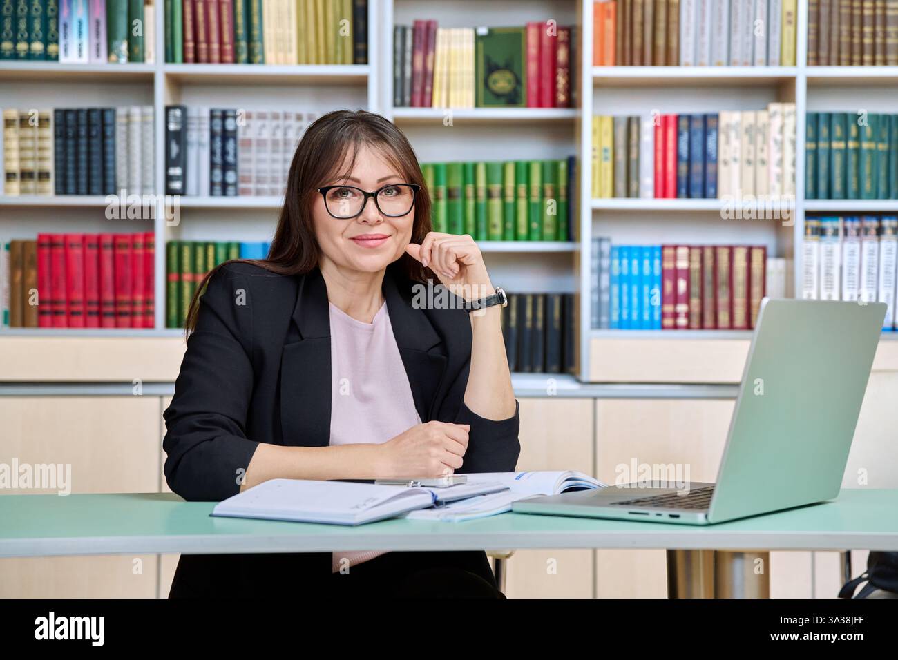 Porträt einer Lehrerin mittleren Alters mit Laptop in der Bibliothek Stockfoto
