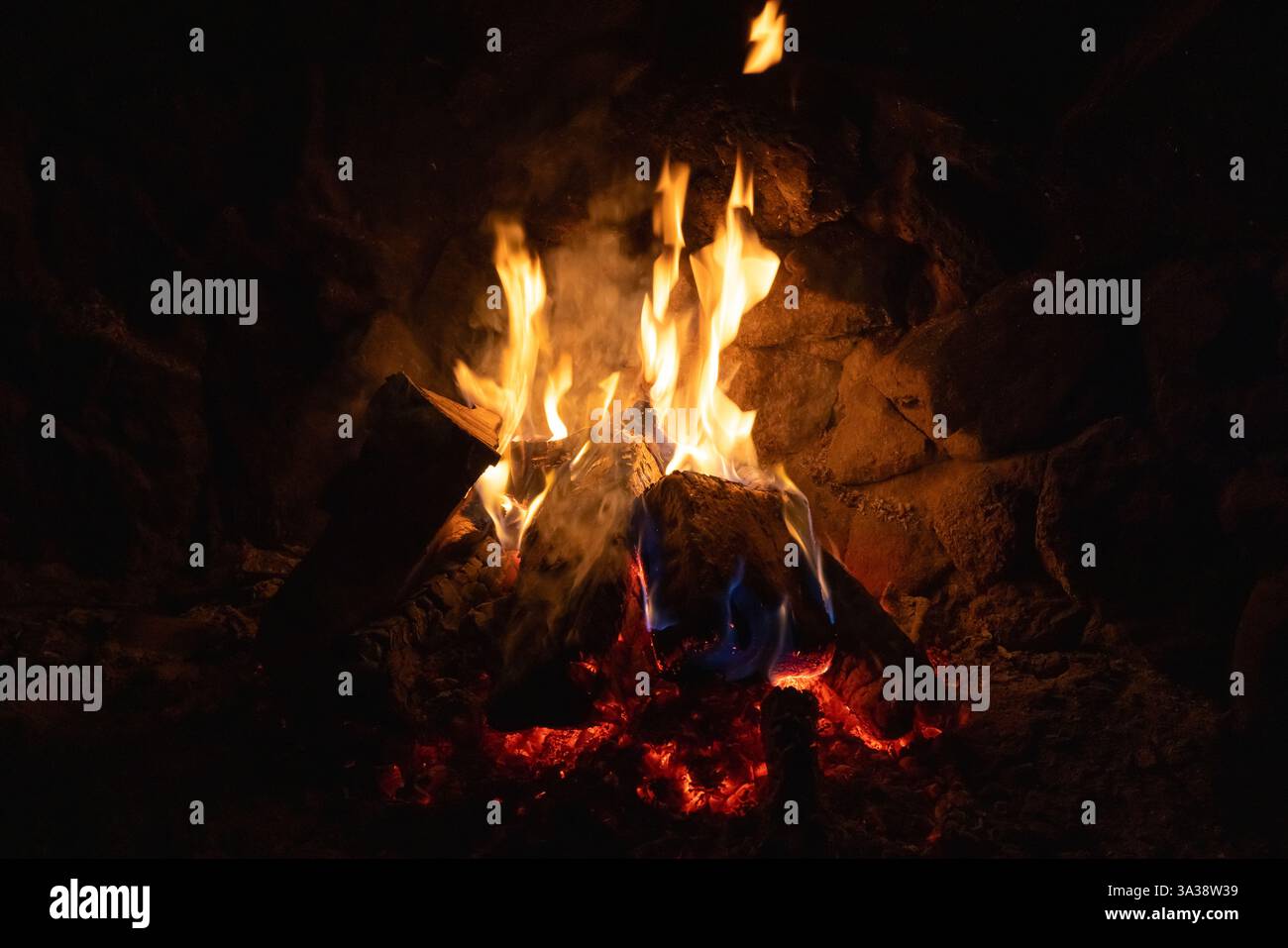 Ein Blick aus der Nähe auf ein Lagerfeuer mit lebhaften Flammen und glühender Glut umgeben von Felsen, die eine warme und gemütliche Atmosphäre schaffen Stockfoto Ein Blick aus der Nähe auf ein Lagerfeuer mit lebhaften Flammen und glühender Glut umgeben von Felsen, die eine warme und gemütliche Atmosphäre schaffen Stockfoto