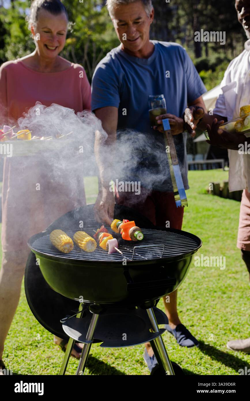 Verschiedene Seniorfreunde genießen Barbecue im Freien, grillen Gemüse und treffen sich im Hinterhof Stockfoto