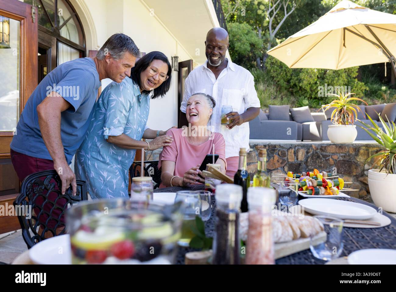 Ältere Freunde genießen ein Mittagessen im Freien, lachen und erzählen Geschichten bei einem Treffen im Hinterhof Stockfoto