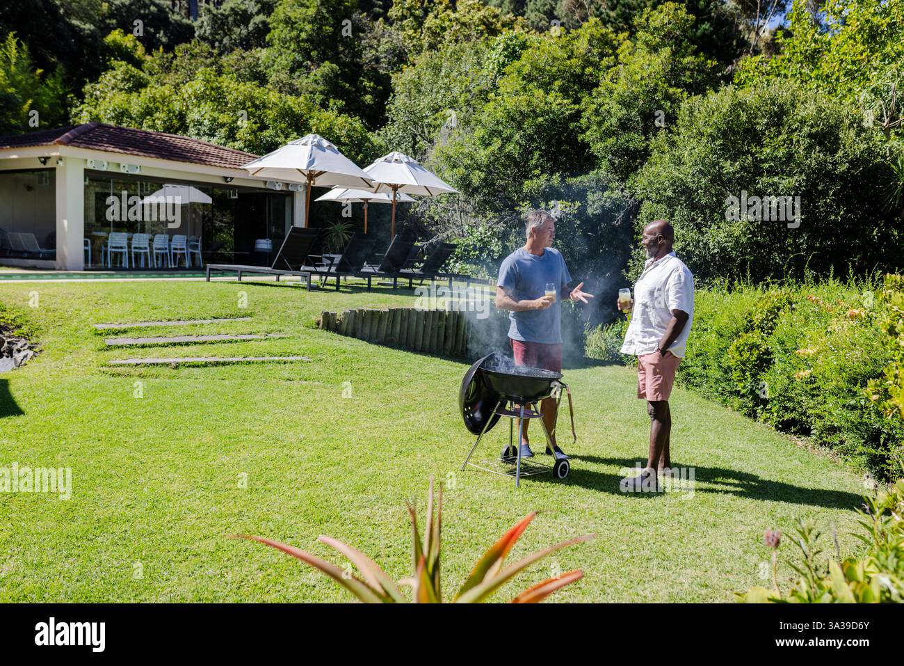 Zwei Männer grillen und plaudern im sonnigen Hinterhof, genießen Freizeit im Freien, Kopierraum Stockfoto