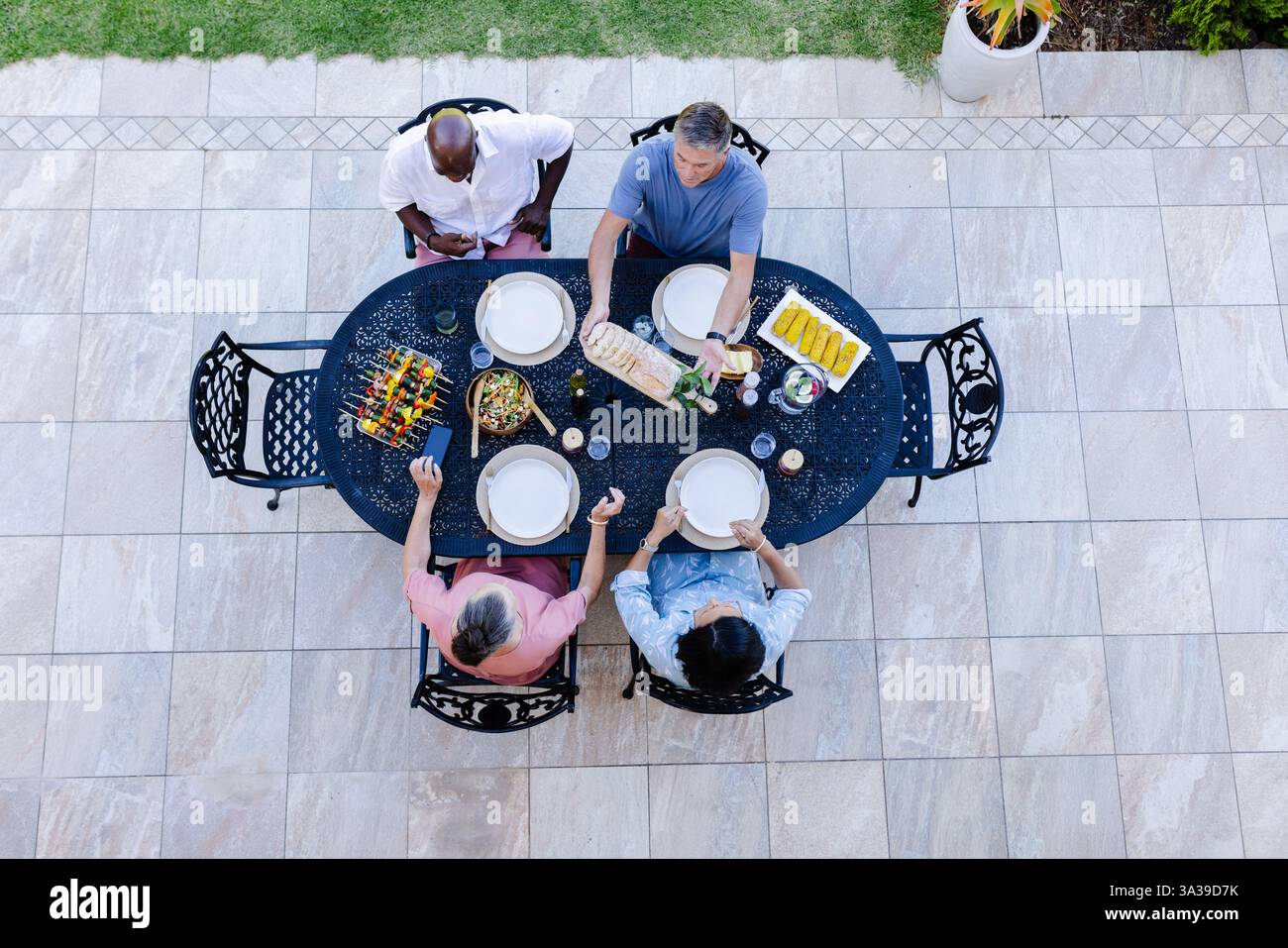 Seniorenfreunde genießen ein Abendessen im Freien, teilen Essen und unterhalten sich rund um den Terrassentisch Stockfoto