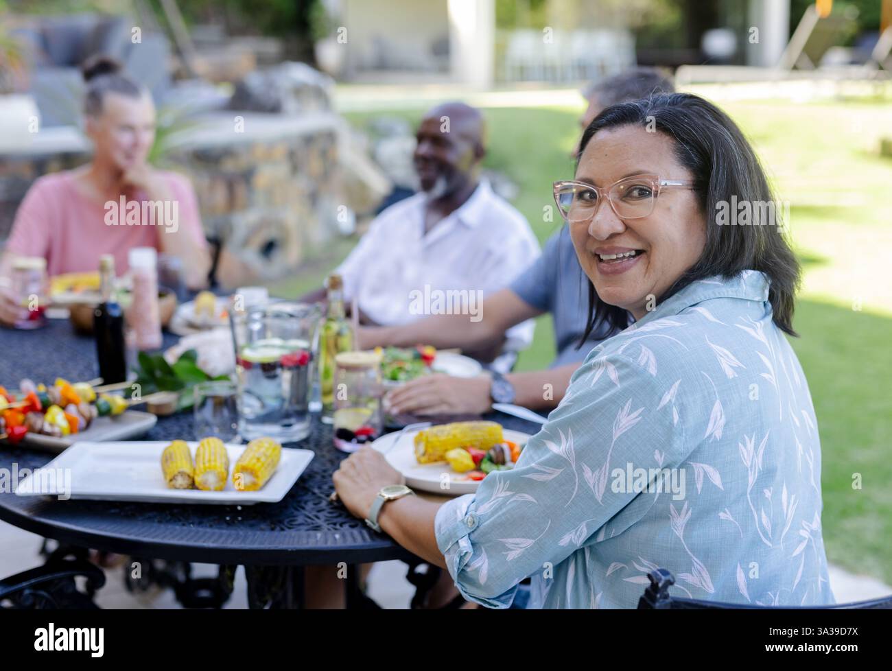 Lächelnde Seniorin genießt ein Mittagessen im Freien mit älteren Freunden, teilt Essen und lacht Stockfoto