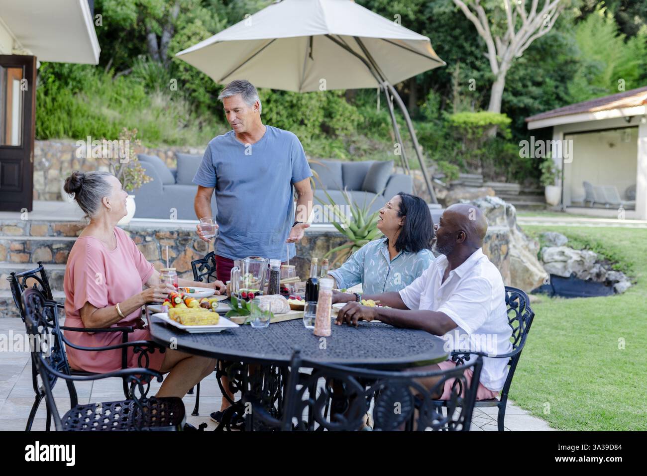 Ältere Freunde genießen Mittagessen im Freien, lachen und unterhalten sich am Gartentisch im Hinterhof Stockfoto