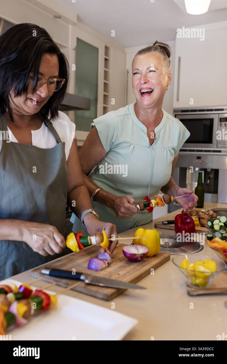Zwei Frauen bereiten Gemüsespieße in der modernen Küche zu, die gerne zusammen kochen Stockfoto