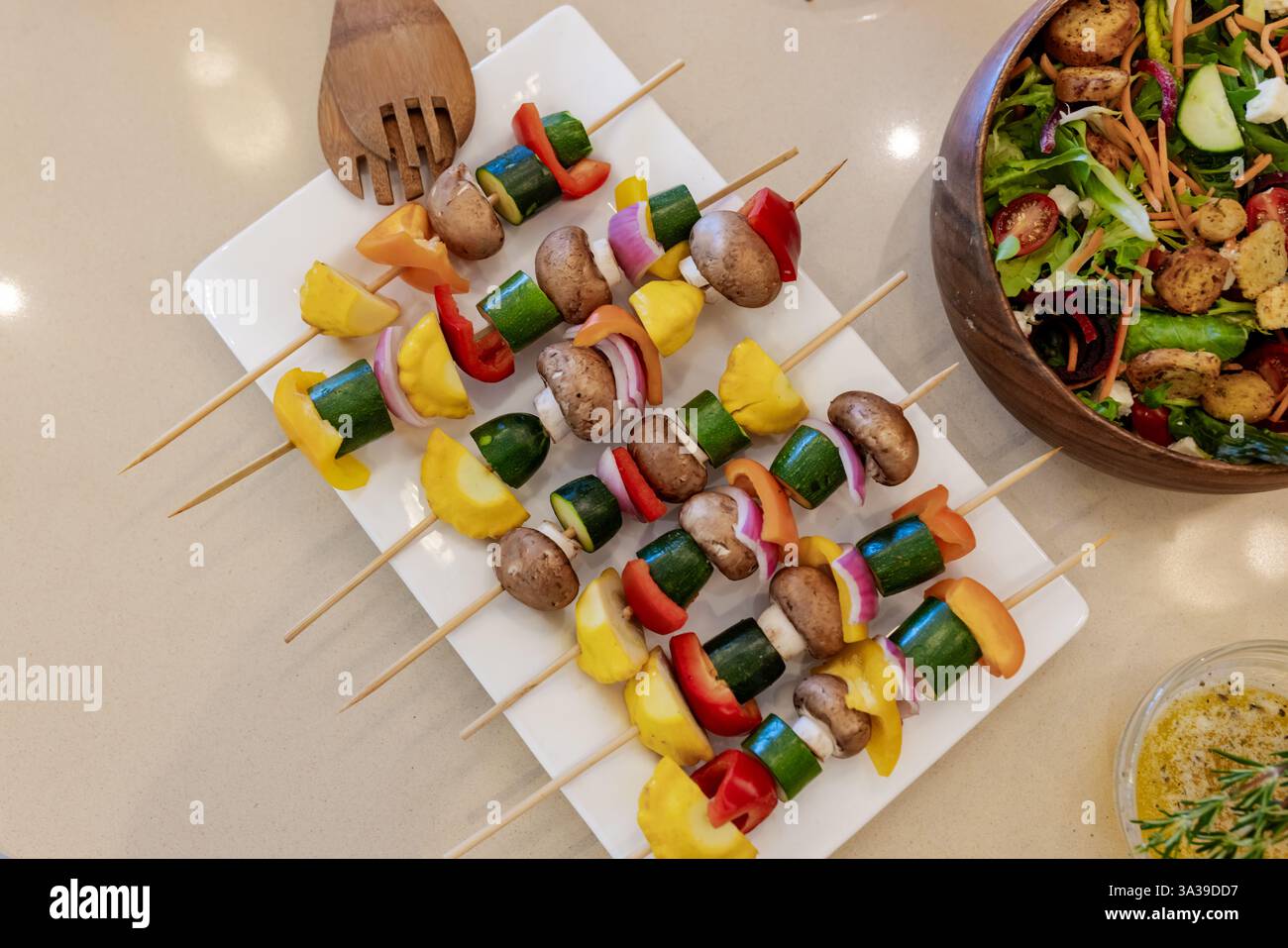 Bunte Gemüsespieße auf Platte neben frischem Salat in Schüssel Stockfoto