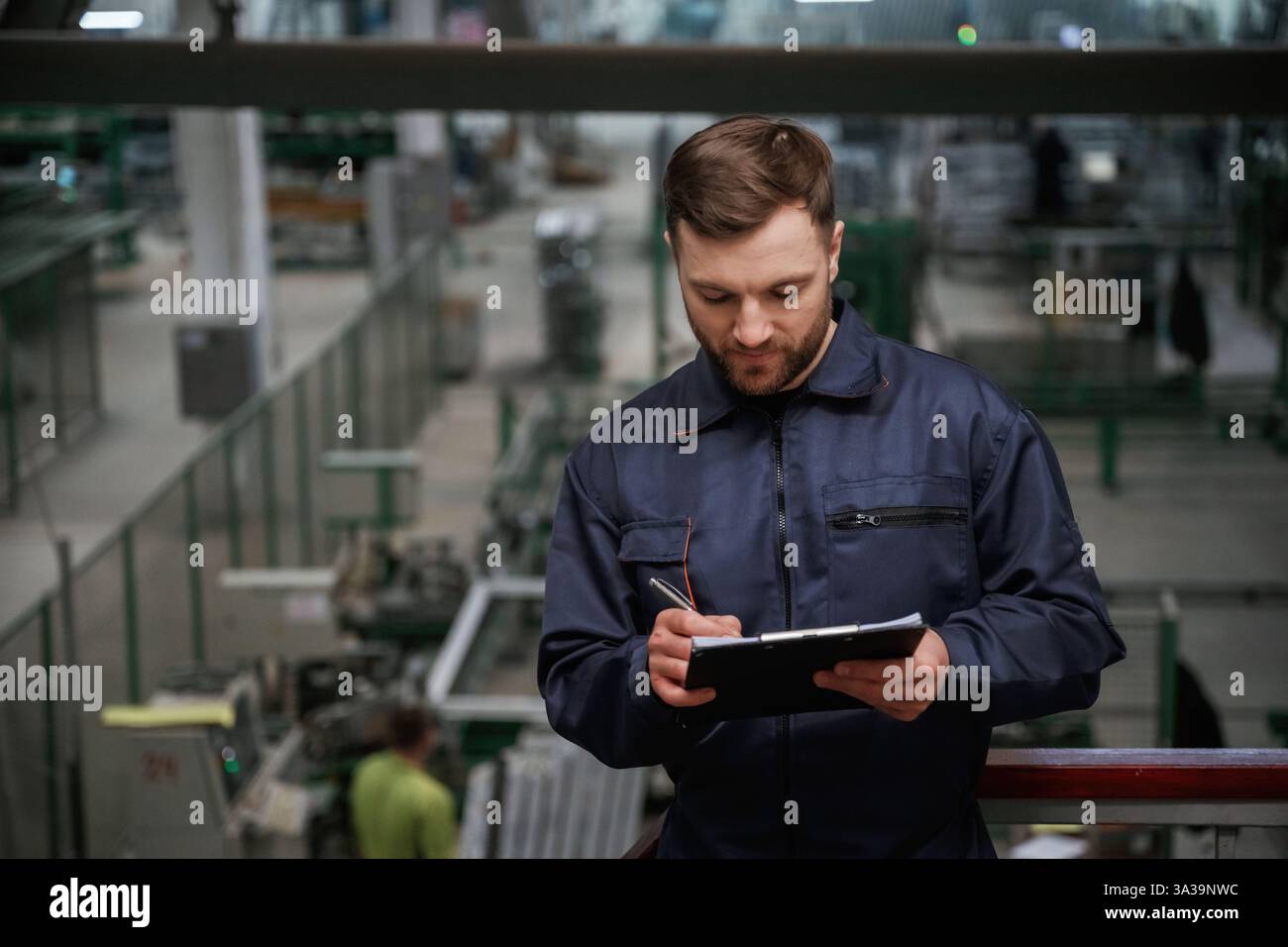 Schreiben von Informationen in den Notizblock. Fabrikarbeiter ist mit Schutzhelm drinnen. Stockfoto