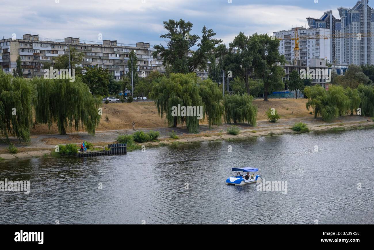 Ein kleines Boot gleitet ruhig über den Fluss Dnipro, während üppiges Grün an der ruhigen Küste vorbeiführt und einen Moment der Ruhe einnimmt. Stockfoto