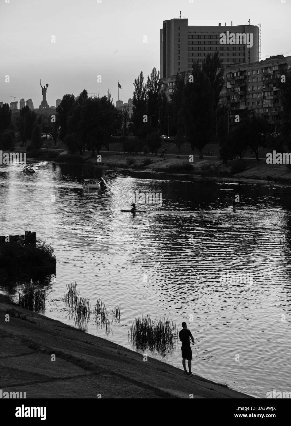 Der Abend strahlt ein sanftes Leuchten über dem berühmten Mutter-Ukraine-Denkmal aus, während die Einheimischen ruhige Momente am Fluss Dnipro in Kiew genießen. Stockfoto