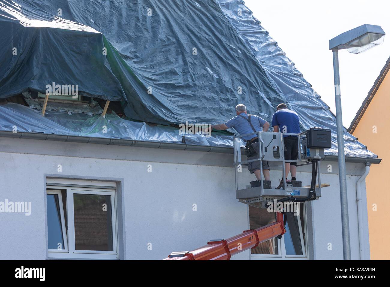 Neuwied, 3. Juni 2022: Zwei Dachdecker auf einer Höhenplattform decken ein Dach mit einer Kunststoffleinwand ab Stockfoto