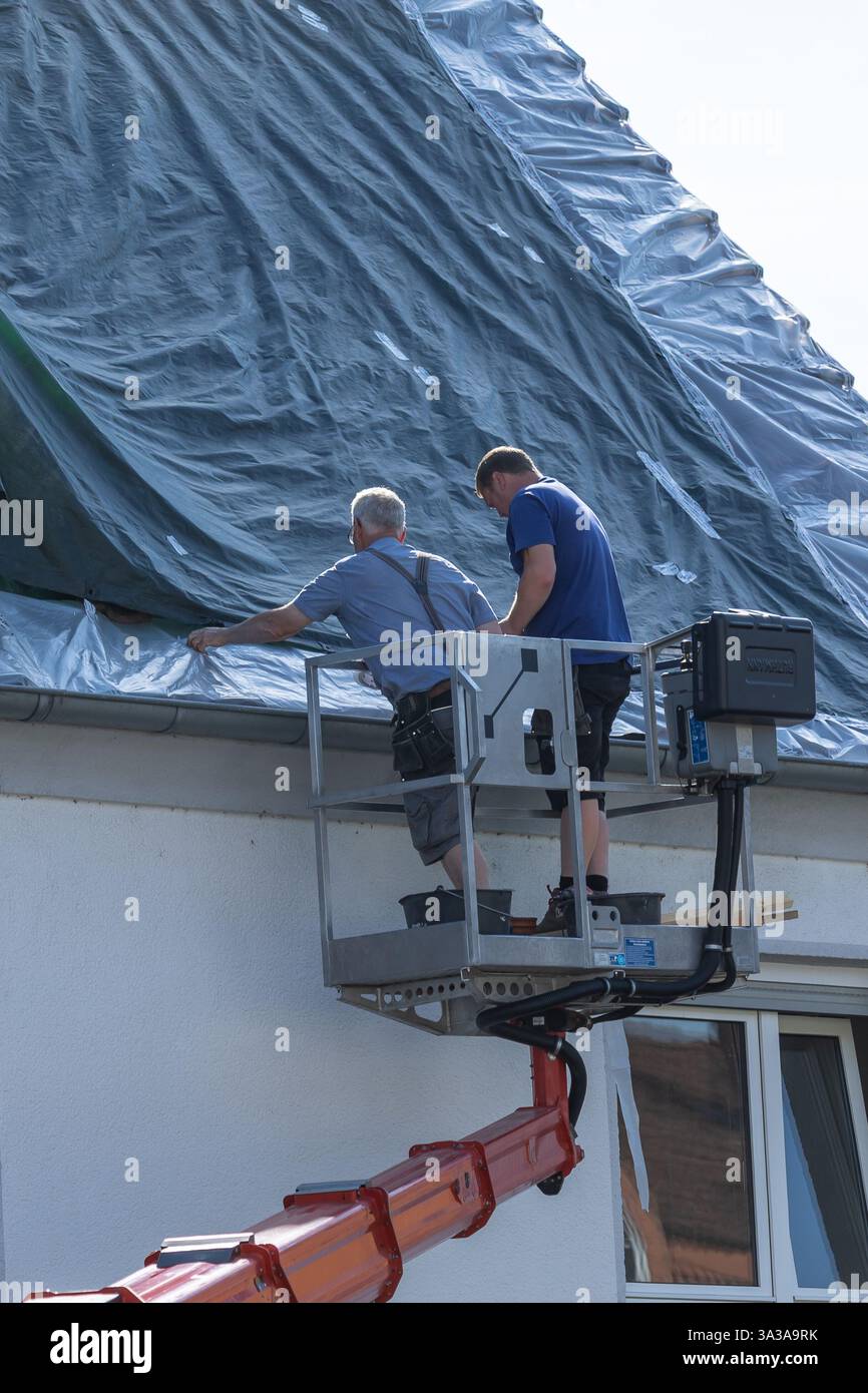 Neuwied, 3. Juni 2022: Zwei Dachdecker auf einer Höhenplattform decken ein Dach mit einer Kunststoffleinwand ab Stockfoto