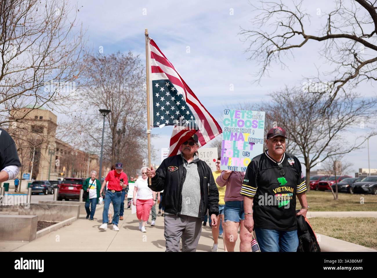 INDIANAPOLIS, INDIANA - 14. MÄRZ: Ein Vietnam-Veteran trägt eine umgedrehte amerikanische Flagge als Zeichen der Not, während US-Militärveteranen und ihre Unterstützer gegen die Kürzungen der Trump-Regierung am Department of Veterans Affairs (VA) und andere Veränderungen, die Veteranen und das Militär am 14. März 2025 betreffen, vor dem Indiana Statehouse in Indianapolis, Indiana, protestieren. Der inoffizielle Protest an der Basis wurde durch einen Flyer ausgelöst, der von der 50501-Bewegung gepostet und von Veteranen in den Vereinigten Staaten online entdeckt wurde. Quelle: Jeremy Hogan/Alamy Live News Stockfoto