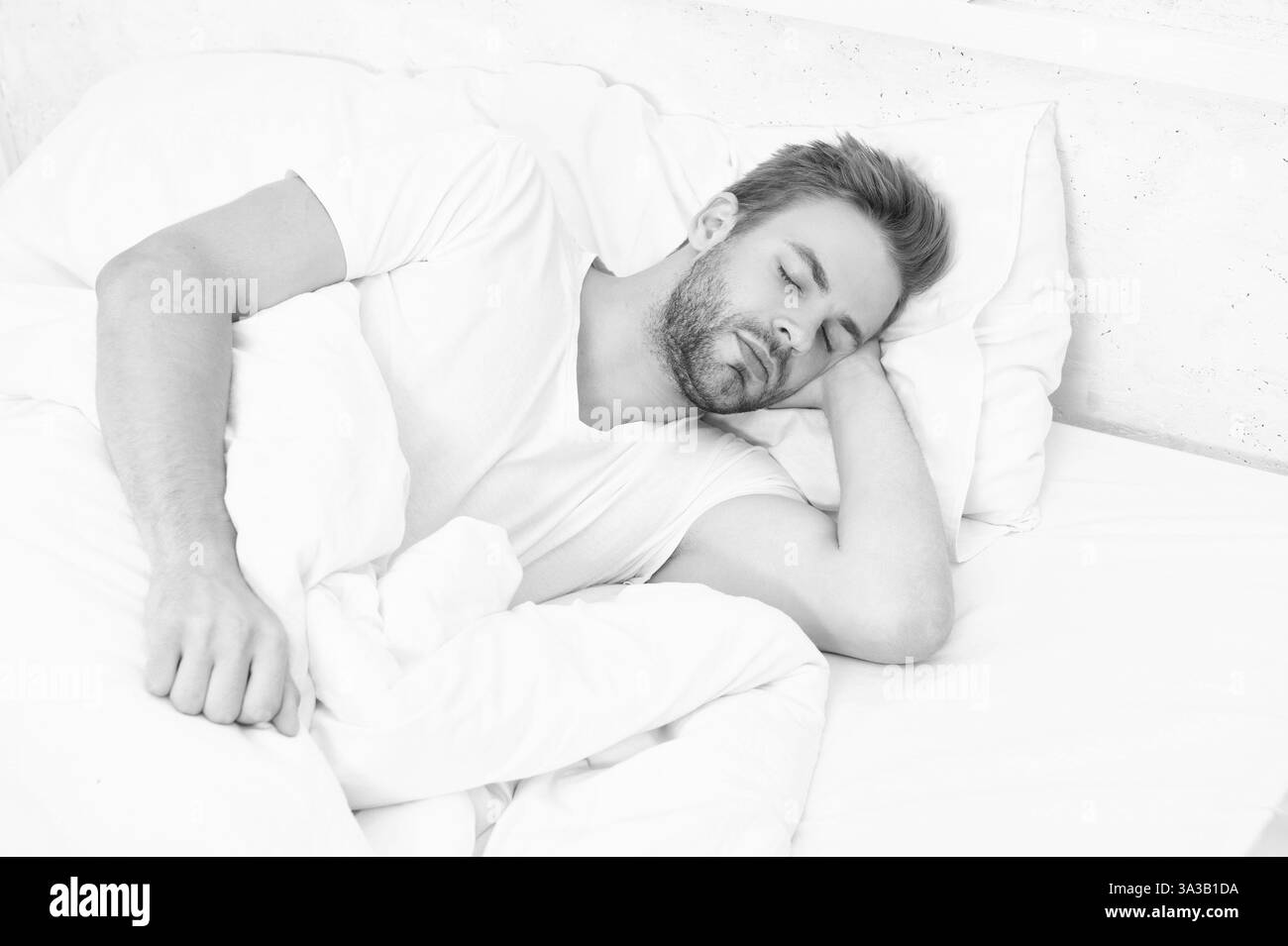 Schläfriger Mann, der auf dem Bett liegt und im weißen Schlafzimmer schläft. Schlafender junger Mann, der schläft. Erholsame Ruhe in einem komfortablen Bett. Mit geschlossenen Augen liegen. Tiefe männlich Stockfoto