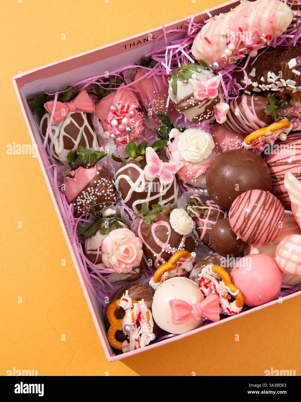 Exquisite rosafarbene Geschenkbox mit wunderschön verzierten Erdbeeren mit Schokoladenüberzug und verschiedenen Gourmet-Pralinen Stockfoto
