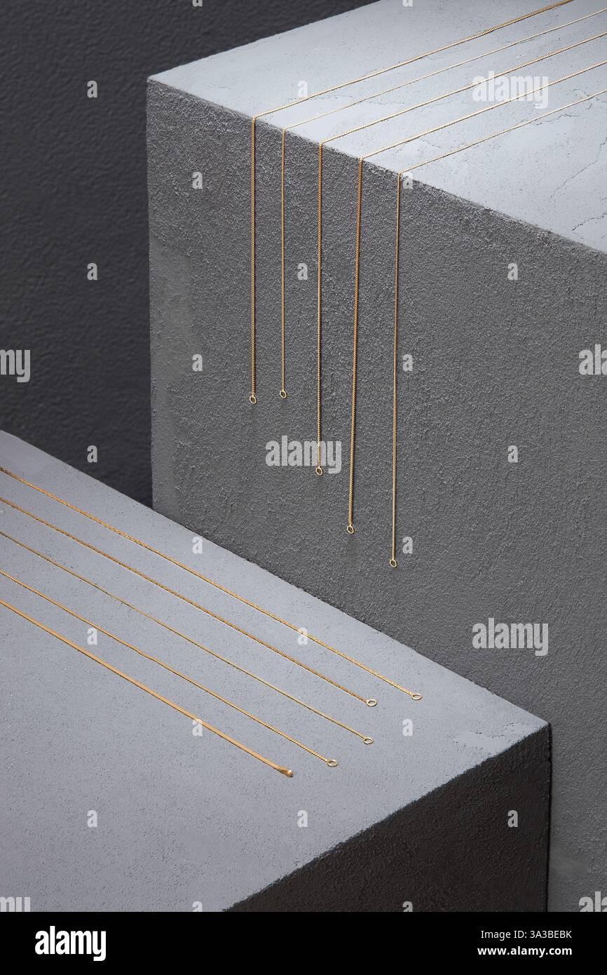 Einfache goldene Kettenketten, die auf grauen Betonblöcken angeordnet sind. Minimalistische und elegante Schmuckpräsentation Stockfoto