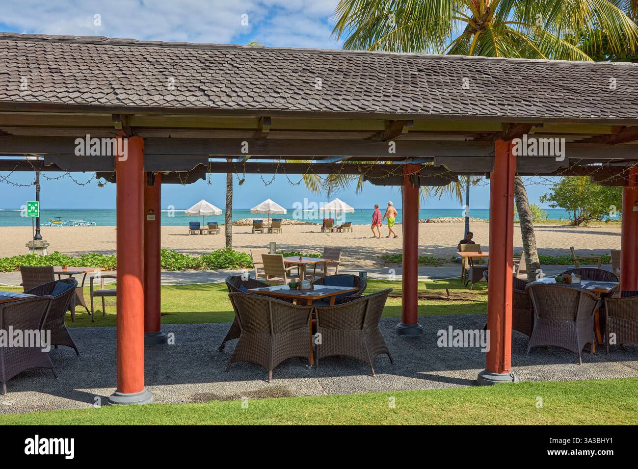 Blick auf den sandigen Jerman Beach (Pantai Jerman) durch eine überdachte Terrasse eines leeren Strandrestaurants. Kuta, Bali, Indonesien. Stockfoto