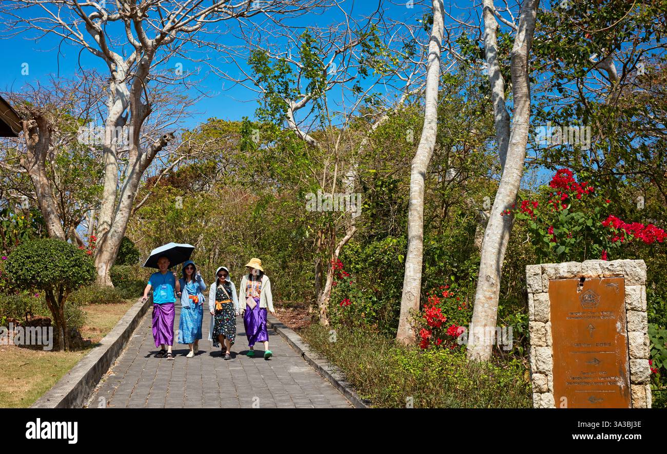 Besucher in Sarongs spazieren durch den Garten des Uluwatu-Tempels (Pura Luhur Uluwatu). Bukit-Halbinsel, Bali, Indonesien. Stockfoto