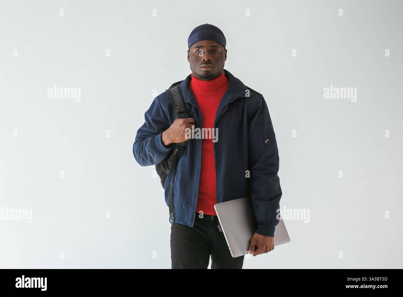 Silberfarbener Laptop in der Hand. Schwarzer Mann mit Kappe ist im Studio vor weißem Hintergrund. Stockfoto