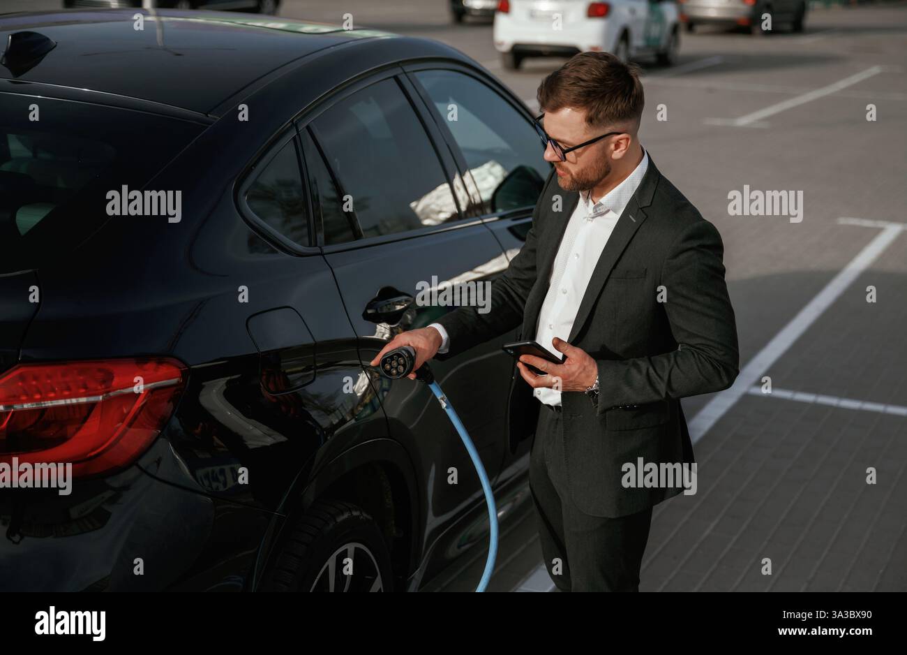 Konzept für umweltfreundliche Energie, Laden. Geschäftsmann im Anzug ist draußen in der Nähe seines schwarzen Autos. Stockfoto
