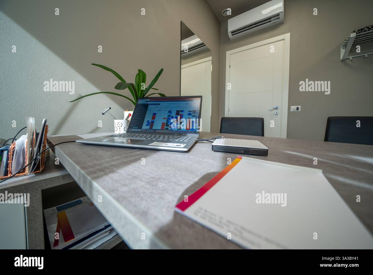 Minimalistisches Büro mit elegantem Schreibtisch, komfortablem Stuhl und offenem Laptop. Stockfoto