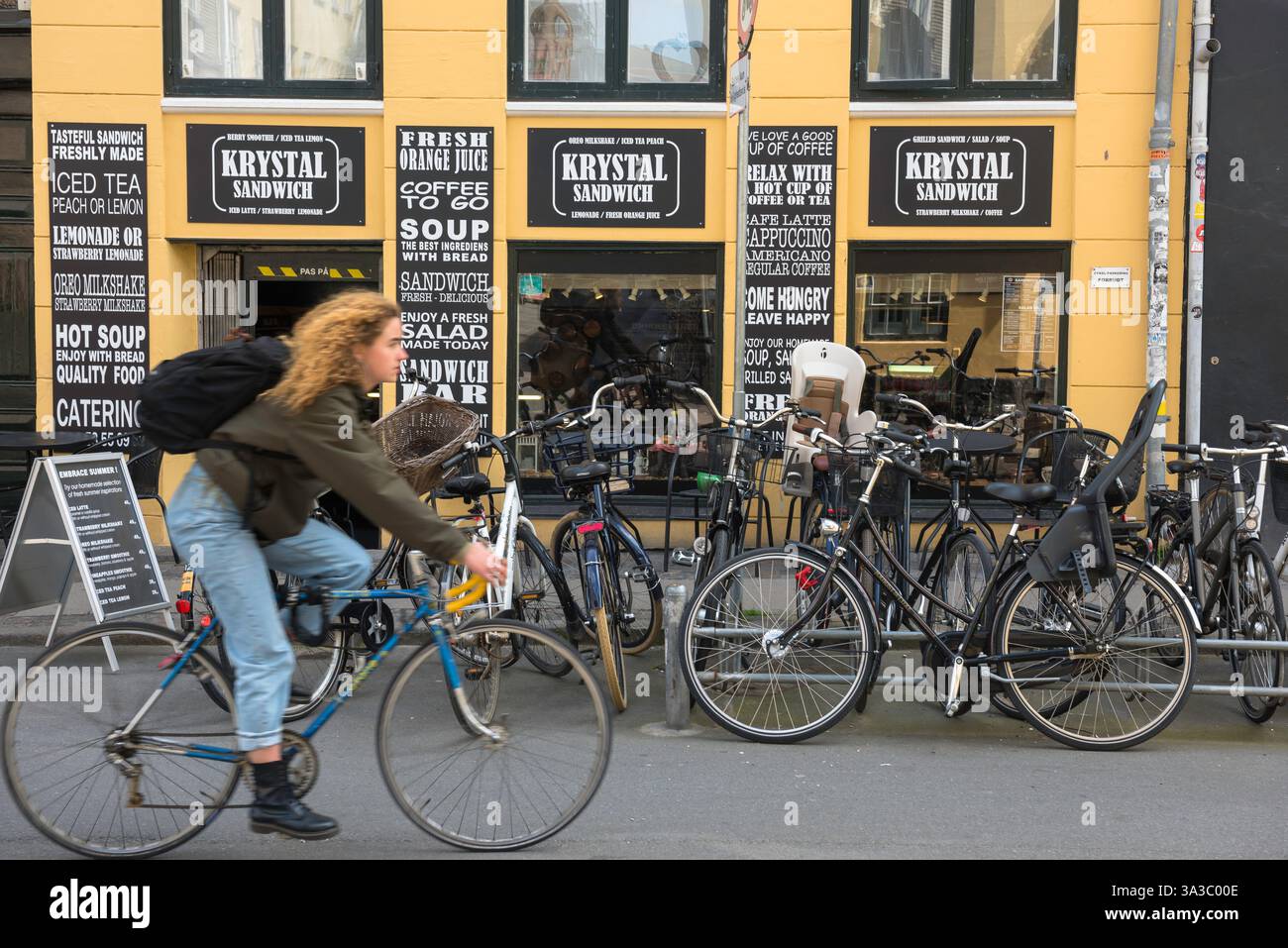 Mit dem Fahrrad durch Europa, Blick auf eine junge Frau, die an einer beliebten Sandwich-Bar in der historischen Altstadt von Kopenhagen, Dänemark, vorbeifährt. Stockfoto