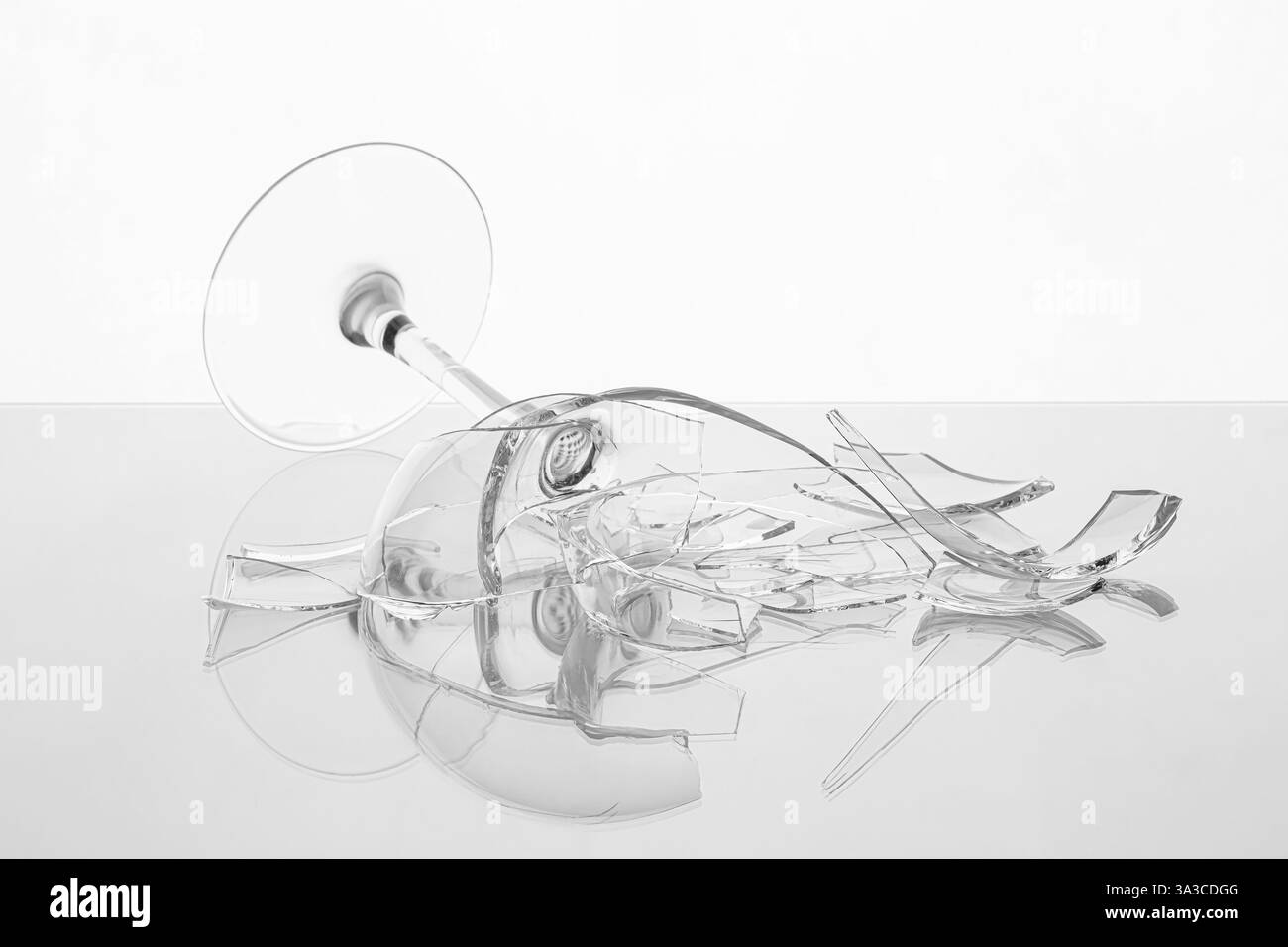 Stücke von zerbrochenem Weinglas auf dem Tisch vor weißem Hintergrund, Nahaufnahme Stockfoto