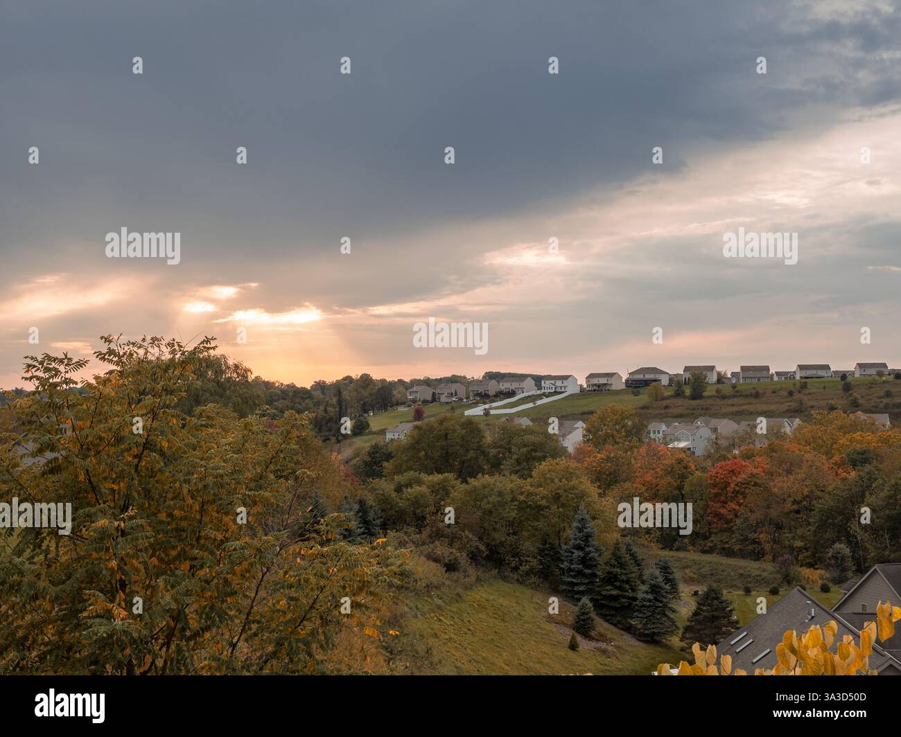 Das Sonnenlicht bricht durch die Wolken, verbreitet warme Strahlen über ein amerikanisches Viertel und taucht die Szene in ein ruhiges, goldenes Herbstglühen. Stockfoto