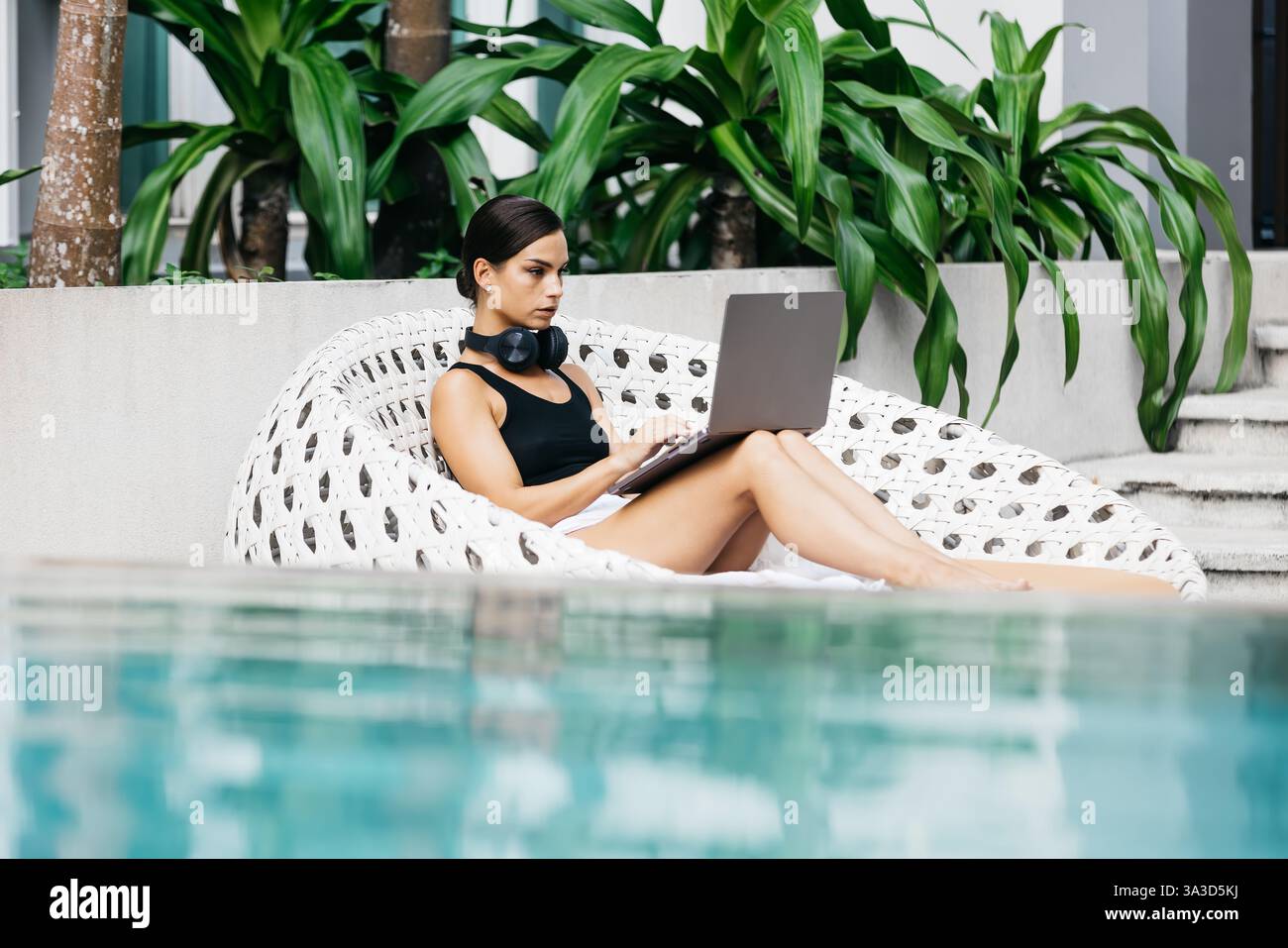 Frau mit Kopfhörern, die in einem tropischen Umfeld arbeitet oder studiert. Das Konzept von Remote-Arbeit, Flexibilität und Business in jeder Umgebung. Stockfoto