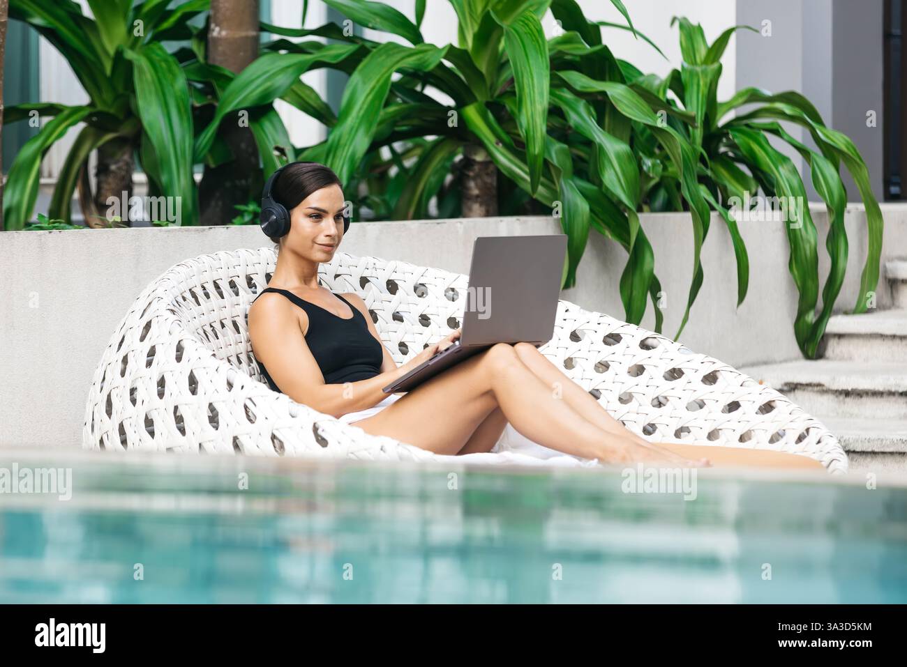 Frau mit Kopfhörern, die in einem tropischen Umfeld arbeitet oder studiert. Das Konzept von Remote-Arbeit, Flexibilität und Business in jeder Umgebung. Stockfoto