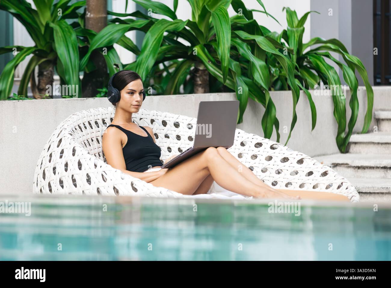 Frau mit Kopfhörern, die in einem tropischen Umfeld arbeitet oder studiert. Das Konzept von Remote-Arbeit, Flexibilität und Business in jeder Umgebung. Stockfoto